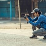A young man crouching to take photos with his DSLR camera in an urban environment.